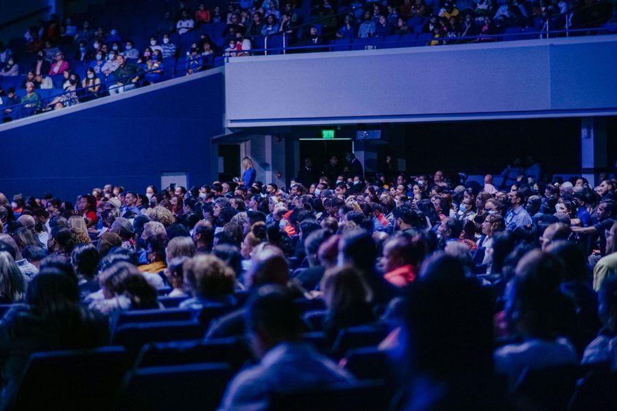 Large audience seated in a darkened hall for a presentation